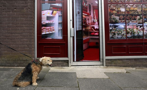 A man walks his dog past a vacant shop, with graphics pasted to the outside to make it look like working butchers shop, in the village of Belcoo, Northern Ireland